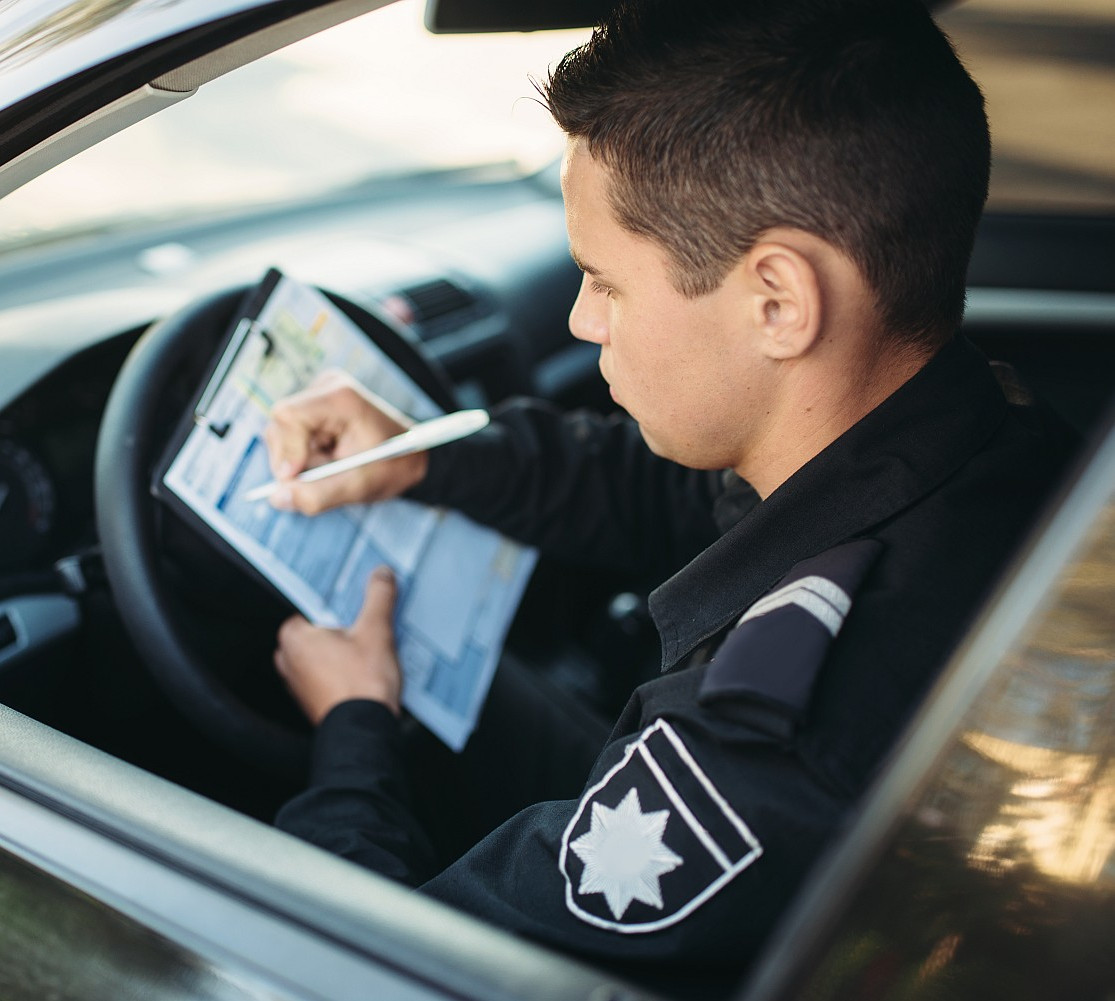 hombre policia sentado coche escribe multa recortado